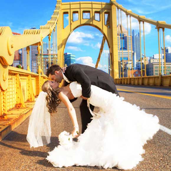 Groom kissing bride on street by bridge